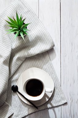 Beyazlar içinde minimalist bir hayat. Bir fincan kahve, hafif bir peçete ve beyaz bir tencerede sulu bir bitki, yazacak bir yeri olan bir lamba masasında.