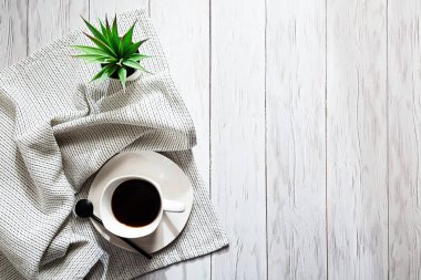 Beyazlar içinde minimalist bir hayat. Bir fincan kahve, hafif bir peçete ve beyaz bir tencerede sulu bir bitki, yazacak bir yeri olan bir lamba masasında.