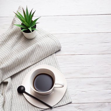 Beyazlar içinde minimalist bir hayat. Bir fincan kahve, hafif bir peçete ve beyaz bir tencerede sulu bir bitki, yazacak bir yeri olan bir lamba masasında.