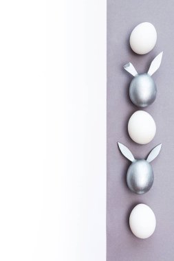 Paskalya için minimum konsept. Tavşan kulaklı yumurtalar beyaz ve gri arka planda renkli gümüş ve beyaz yumurtalardır.