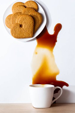 Kalp şeklinde modern bir hayat tabakta zencefilli kurabiye ve masaya dökülmüş bir fincan kahve..