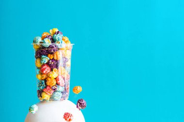 Mavi arka planda şeffaf bir bardakta renkli patlamış mısırlı yaratıcı kompozisyon. Kopyalama alanı olan modern soyut yaşam