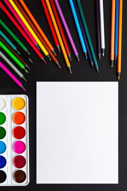 Boş kağıt, renkli kalemler ve boyalar. Model yap, düz yat. Siyah arkaplandaki kırtasiyenin parlak hayat sahnesi.