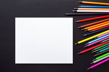 Boş kağıt ve renkli kalemler. Taklit et, düz yat. Siyah arkaplandaki kırtasiyenin parlak hayat sahnesi.