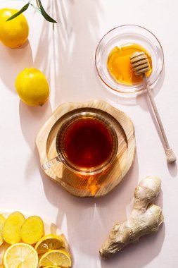 Bir fincan zencefilli çay, bal, limon ve zencefil kökü, pembe arka planda yatıyordu. Modern sağlık konsepti. Vejetaryen, sağlıklı yiyecekler, bağışıklığı arttırmak..