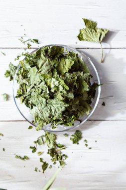 Beyaz ahşap bir masada cam bir tabakta kurutulmuş üzümlü yapraklar. Organik, doğal, kuru bitki çayıyla kompozisyon