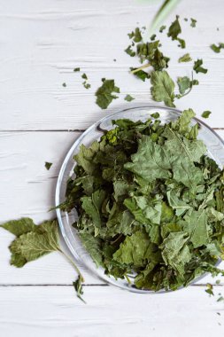 Beyaz ahşap bir masada cam bir tabakta kurutulmuş üzümlü yapraklar. Organik, doğal, kuru bitki çayıyla kompozisyon