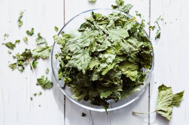 Beyaz ahşap bir masada cam bir tabakta kurutulmuş üzümlü yapraklar. Organik, doğal, kuru bitki çayıyla kompozisyon