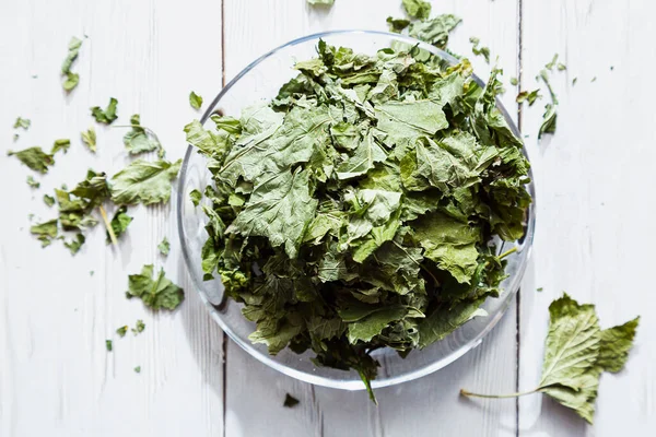 Beyaz ahşap bir masada cam bir tabakta kurutulmuş üzümlü yapraklar. Organik, doğal, kuru bitki çayıyla kompozisyon
