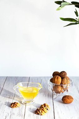 Ceviz yağı ve beyaz ahşap bir masada bir demet fındık. Yağ ve cevizli modern cam kase, zeytin dalı ve uzay kopyası..