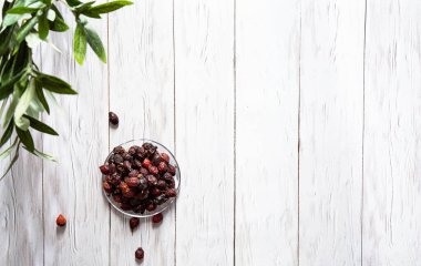 Beyaz ahşap bir masada cam bir tabakta kurumuş gül kalçası meyvesi. Geleneksel ilaç kavramı. Organik gül kalçası, antioksidan, C vitamini kaynağı, bağışıklık koruması. Süperyiyecekler.