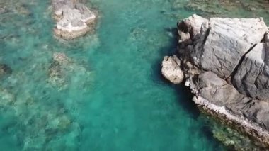 Gök mavisi okyanus ve kayalık deniz kayalıklarının nefes kesici manzarası. İnsansız hava aracı turkuaz okyanusun üzerinden kayaların arkasına doğru uçuyor..