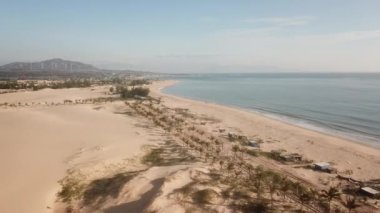 The drone flies going through the sand dunes towards the sea. Aerial Drone Footage high above the beach with the ocean.