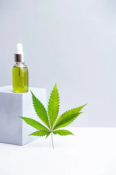 Cosmetics CBD oil and leaves of cannabis. Modern still life of glass bottles with Hemp oil, THC tincture, hemp leaves and cube geometric shape 