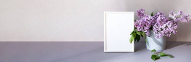 Minimalist iç mekândaki fotoğraf çerçevesini düzenle. Beyaz çerçeveli ve leylak buketli modern natürmort. Moda ev dekorasyonu kavramı. Pastel renklerde pankart.