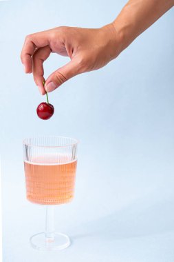 Summer, ferahlatıcı içecek konsepti. Bir bardak pembe şampanyayla bir kadın eli. Minimalistler hala çilekli limonata ve kirazla yaşıyor. Poster, boşluğu kopyala 