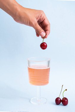 Summer, ferahlatıcı içecek konsepti. Bir bardak pembe şampanyayla bir kadın eli. Minimalistler hala çilekli limonata ve kirazla yaşıyor. Poster, boşluğu kopyala 