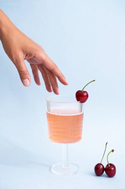 Summer, ferahlatıcı içecek konsepti. Bir bardak pembe şampanyayla bir kadın eli. Minimalistler hala çilekli limonata ve kirazla yaşıyor. Poster, boşluğu kopyala 