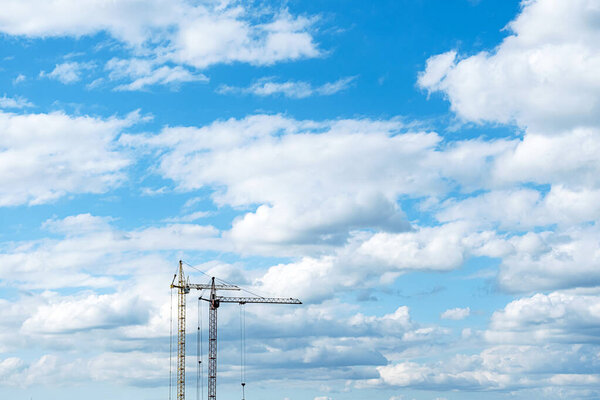 Two construction cranes against the blue cloudy sky. Tower crane for lifting loads in the construction of buildings. Industrial background with place for text or advertisement.