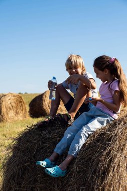 Kız ve erkek samanlıkta eğleniyor. Kırsalda yaz mevsimi. Sahadaki sevimli çocuklar. Mutlu çocukluk kavramı.