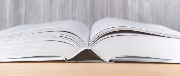 The book lies on a wooden table. Educational literature in the library in the open form. Wide and narrow banner in soft beige shades on a light textured background.