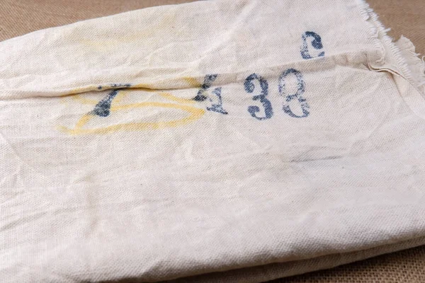 An old cloth bag for storing bulk grocery products. Dense material with serial numbers applied in black and yellow paint. Wrinkled and frayed item for use in embroidery and design.