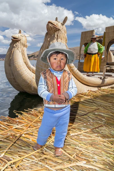 Puno, Perú - circa junio 2015: Niño pequeño en ropa tradicional y canoa en Uros isla flotante y pueblo en el lago Titicaca cerca de Puno, Perú — Foto de Stock