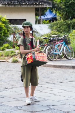 Yangshuo, China - circa July 2015: Chinese young pioneer girl sells food or souvenirs on the streets of tourist town Yangshuo on the banks of Li river in  China