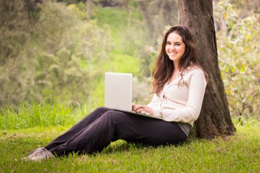 Parkta bir dizüstü bilgisayar kullanan genç güzel kadın