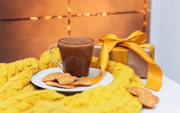 a cup of cocoa and cookies on a white plate on a white table and a yellow knitted blanket