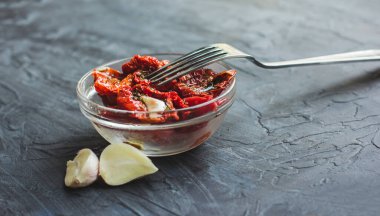 Sarımsaklı ve zeytinyağlı kurutulmuş domatesler gri bir masanın arka planında.