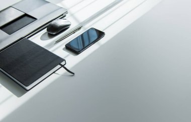 Bilgisayarı, akıllı telefonu, not defteri ve kalemi olan beyaz ofis masası. Fotokopi alanı olan üst görünüm, düz. İş ve ev kavramında çalışma