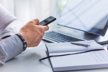 Masada elinde telefonla oturan bir adamın resmi. Not defterinin ve tükenmez kalemin yanında.