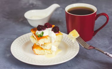 Beyaz tabakta süzme peynir güveci ve gri arka planda bordo bardakta çay.