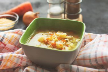 Yeşil tabakta sebzeli tavuk çorbası, siyah arka plan.