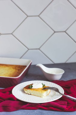 Beyaz tabakta süzme peynir güveci ve gri arka planda bordo bardakta çay.