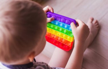 Sarışın çocuk gökkuşağıyla oynuyor. Kıpır kıpır. Kabarcık hareketli duyusal oyuncağı itin. Yıkanabilir ve yeniden kullanılabilir stres atma oyuncağı. Özel ihtiyaçları olan çocuklar için stres önleyici bir oyuncak. Ruh sağlığı konsepti 