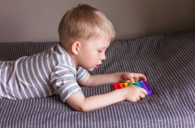 Sarışın çocuk gökkuşağıyla oynuyor. Kıpır kıpır. Kabarcık hareketli duyusal oyuncağı itin. Yıkanabilir ve yeniden kullanılabilir stres atma oyuncağı. Özel ihtiyaçları olan çocuklar için stres önleyici bir oyuncak. Ruh sağlığı konsepti 