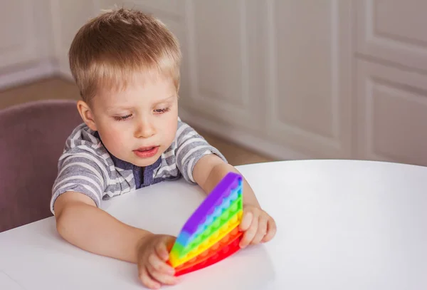 Rubio Chico Jugando Con Arco Iris Pop Fidget Toy Empuje Fotos de stock libres de derechos