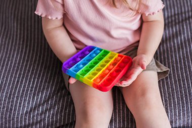 Küçük bir kız oturur ve elinde bir oyuncak tutar gökkuşağı kıpır kıpır bir oyuncak. Kabarcık hareketli duyusal oyuncak silikon stres atma oyuncağı. Özel ihtiyaçları olan çocuklar için stres önleyici oyuncak