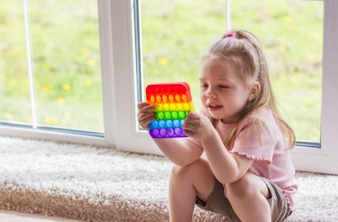 Küçük sarışın kız çocuklar yeni moda duyusal oyuncaklarla oynuyorlar - gökkuşağı patlat onu. Çocuklar ve yetişkinler için stres önleyici oyuncaklar. Renkli oyuncaklar basit gamzeler. Yumuşak yumuşak baloncuk oyuncakları gökkuşağı rengi