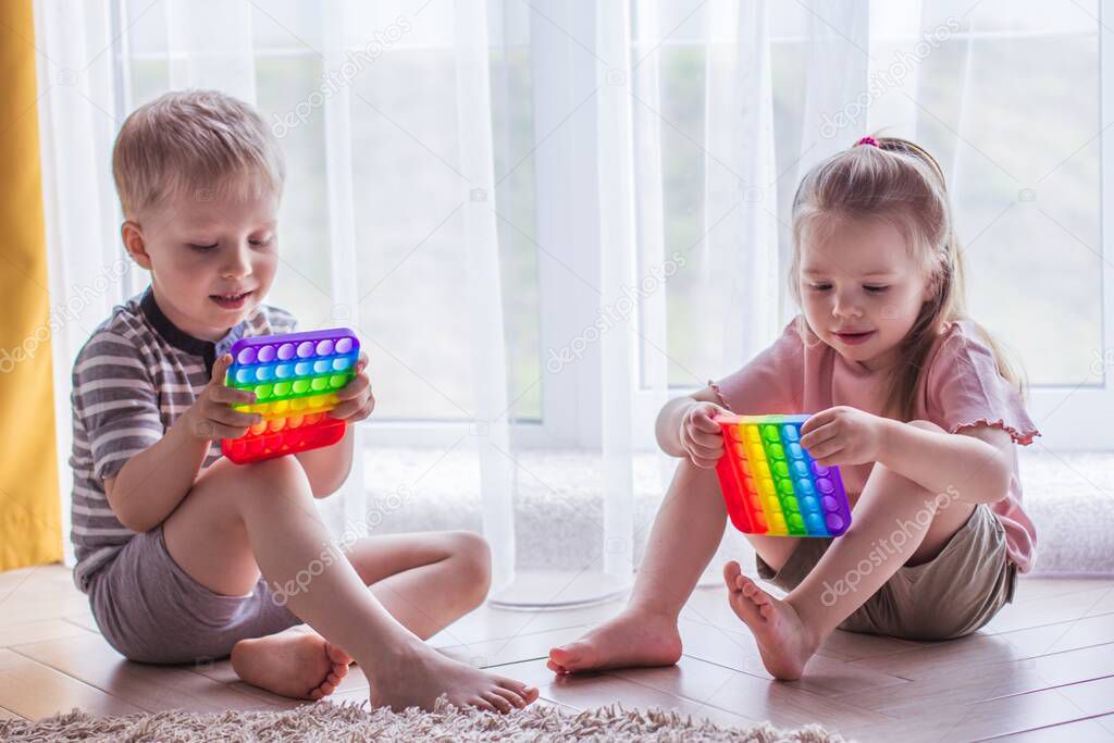 Blonde boy and girl Kids play with pop it sensory toy. Trendy silicon fidgeting game for stressed children and adults. Squishy soft bubble toys. Kid playing with rainbow color pop-it