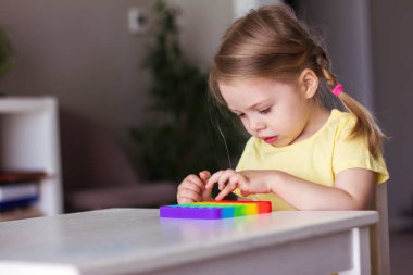 Küçük sarışın kız çocuklar yeni moda duyusal oyuncak gökkuşağıyla oynuyorlar. Çocuklar ve yetişkinler için stres önleyici oyuncaklar. Renkli oyuncaklar basit gamzeler. Yumuşak yumuşak baloncuk oyuncakları gökkuşağı rengi