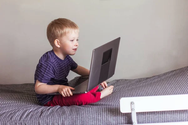 Small Blond Boy Blue Shirt Red Pants Sits Bed Looks — Stock Photo, Image