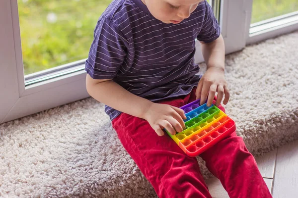 a small blonde boy little blonde boy playing with a modern colorful and bright popit toy Simple dimple. The child with colorful trendy antistress silicon sensory toy