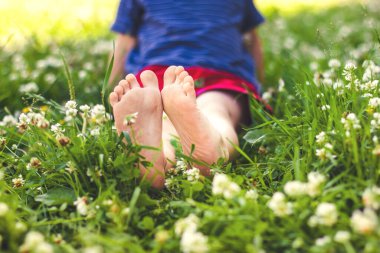 Yeşil, güneşli çimenlerde oturan bir çocuğun bacakları, seçici odaklanma, yumuşak odaklanma.