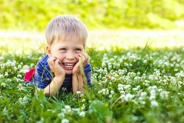 stock image A happy, smiling boy is lying on a green grass lawn. Happy childhood, summer and outdoor recreation