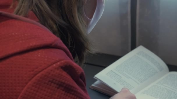 Chica enmascarada leyendo un libro de papel. La educación y la pandemia — Vídeos de Stock