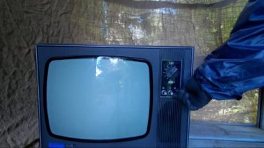 Koruyucu giysili bir adam eski, eski bir TV kanalını değiştiriyor.