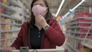 Market arabalı bir kadın yüzüne pembe virüs maskesi takıyor.